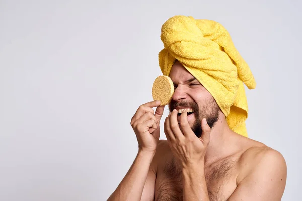 Man met een gele handdoek op zijn hoofd blote schouders spons schone huid gezichtsverzorging lichte achtergrond — Stockfoto