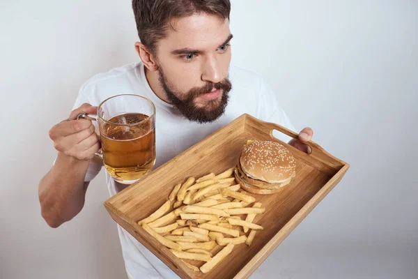 Człowiek z drewnianym taca piwo kubek frytki i hamburger fast food kalorie model biały t-shirt — Zdjęcie stockowe