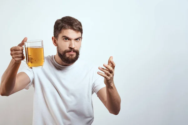 Hombre con una taza de cerveza en sus manos y una camiseta blanca fondo claro bigote barba emociones modelo — Foto de Stock