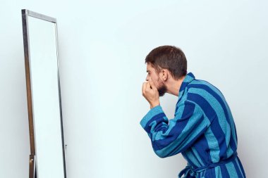 Mavi cüppeli bir adam parlak bir odada, aynada kendini inceliyor.