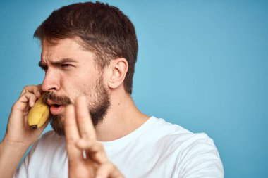 Muzlu bir adam, beyaz bir tişörtle mavi arka planda telefonla iletişim kurarken yakalanır.
