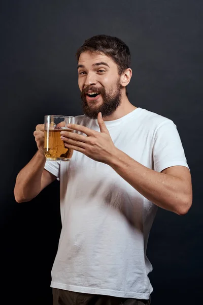 Homme avec une tasse de bière dans ses mains émotions style de vie amusant t-shirt blanc fond sombre isolé — Photo