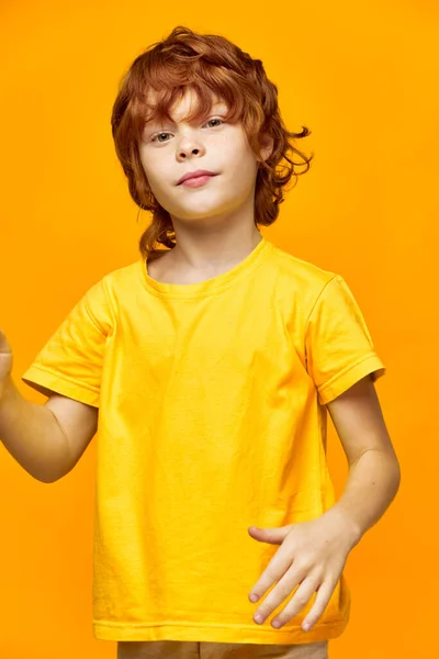 Criança em um amarelo gestos camiseta com as mãos em um fundo isolado e cabelos vermelhos — Fotografia de Stock