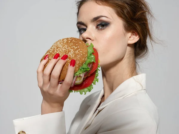 Schöne junge Frau mit Make-up hält einen Hamburger in der Hand — Stockfoto