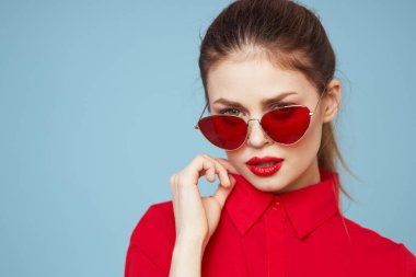 Koyu gözlükleri olan güzel bir kadın parlak makyajlı kırmızı dudaklar mavi arkaplanı büyülüyor.