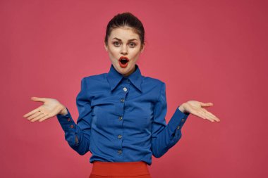 Pembe arka planda mavi gömlekli şık bir kadın. Kırmızı etek duyguları. El hareketleriyle hareket ediyor.