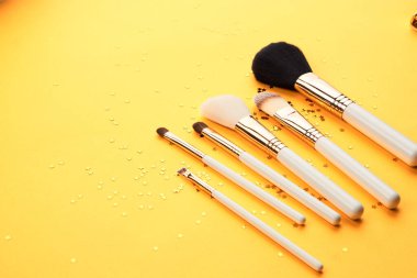 Sarı arka plan profesyonel kozmetik ürünlerinde parıltılı makyaj fırçaları