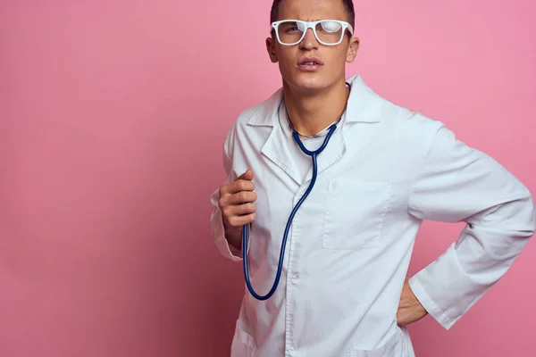 Άντρας γιατρός με ιατρική ρόμπα με στηθοσκόπιο γύρω από το λαιμό του σε ροζ φόντο και γυαλιά στο πρόσωπό του — Φωτογραφία Αρχείου