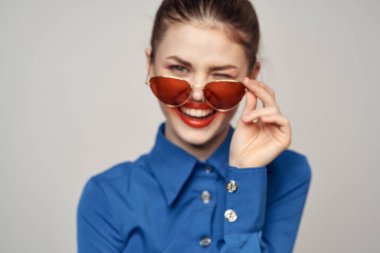 Güneş gözlüklü modaya uygun bir kadın ve elleri açık arka planda beliren mavi bir gömlek.