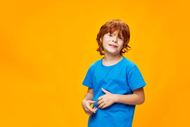 Mavi tişörtlü neşeli kızıl çocuk sarı izole edilmiş arka planda sinsi gülümsemesi olan. 