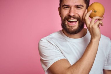 Pembe arka planda, beyaz tişörtlü, turuncu elbiseli genç bir adam. Model ellerle el kol hareketi yapmak eğlenceli.