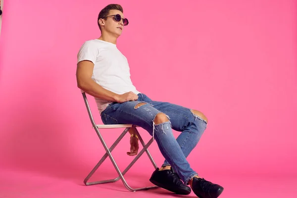 Un hombre se sienta en una silla en una camiseta blanca y jeans de estilo moderno rosa aislado de fondo — Foto de Stock