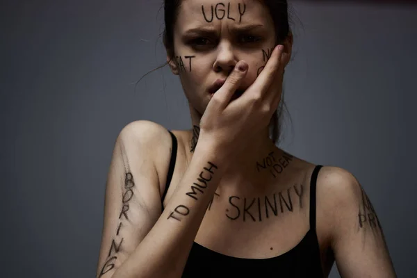 Ображена жінка з розлюченими написами на її тілі торкається себе руками на сірому фоні агресії — стокове фото