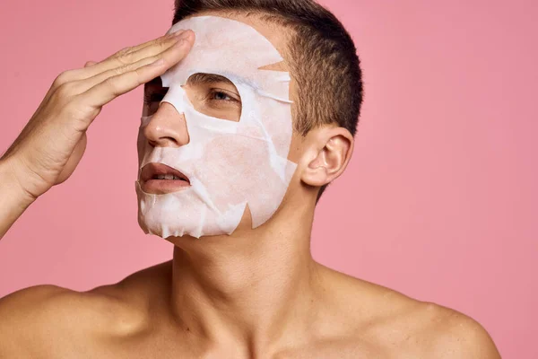 man with cleansing mask against black dots on his face on pink background cropped view and hands near face