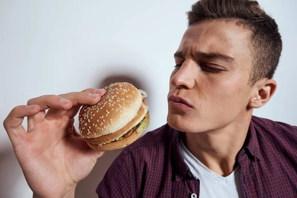 Homem segurando perto rosto hambúrguer dieta comida fome estilo de vida fast food luz fundo — Fotografia de Stock