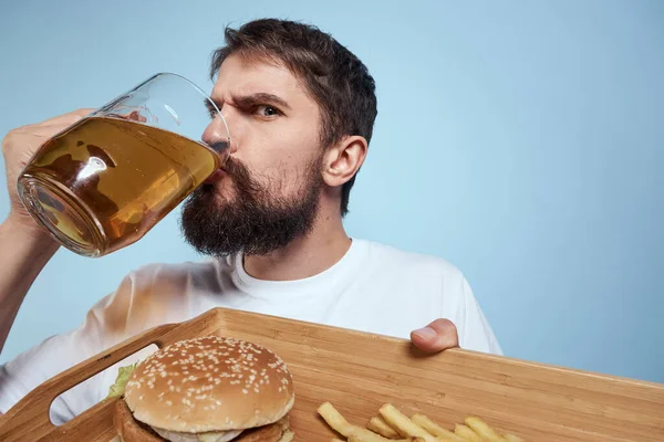 Neşeli adam bira kupa hamburger patates kızartması fast food diyet mavi arka plan yakın plan — Stok fotoğraf