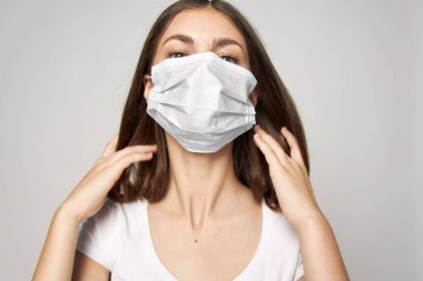 Tıbbi maske takan bir kadın ellerinde beyaz bir tişört tutuyor. 