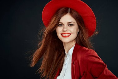 Kırmızı dudaklı güzel bir kadın ceketinde şapkası olan zarif stil cazibesi koyu tenli arka planda.