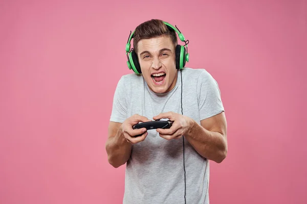 Ein Mann mit einem Steuerknüppel in den Händen Kopfhörer spielen Spiele Unterhaltung Lifestyle weißes T-Shirt rosa Hintergrund — Stockfoto