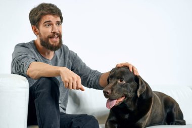 Beyaz bir kanepede siyah köpeği olan bir adam. Arka planda, yakın planda kesilen evcil hayvan insan arkadaş duyguları. Eğlenceli.