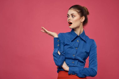 Pembe arka planda mavi gömlekli şık bir kadın. Kırmızı etek duyguları. El hareketleriyle hareket ediyor.