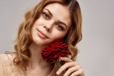 Elinde kırmızı bir gül olan çekici bir kadın açık arkaplanda yakın plan kesilmiş bir portrede.