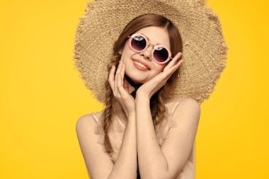 Şapkalı romantik bir kadın sarı arka planda eğleniyor ve güneş gözlüğü siyah kurdele modeli portresi takıyor.
