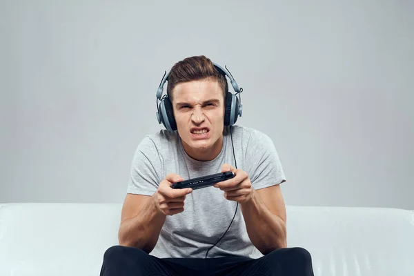 Un hombre con auriculares se sienta en el sofá de la consola de juegos móviles hobby entretenimiento —  Fotos de Stock