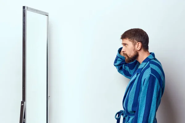 Un homme en robe bleue se regarde dans un miroir dans une pièce lumineuse vue dégagée — Photo