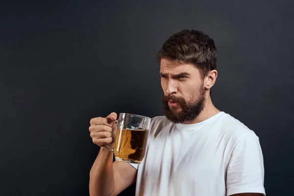 Elinde bir kupa birayla gezen bir adam duyguları olan eğlenceli bir yaşam tarzı beyaz tişört koyu tenha bir arka plan. — Stok fotoğraf