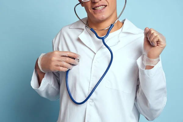 Un trabajador médico con una bata y gafas sostiene un estetoscopio en sus manos sobre un fondo azul vista recortada —  Fotos de Stock