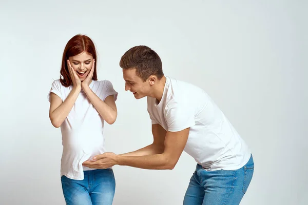 Eine schwangere Frau und ein junger Mann warten auf ein Baby auf einem hellen Hintergrund Emotionen Familienliebe — Stockfoto