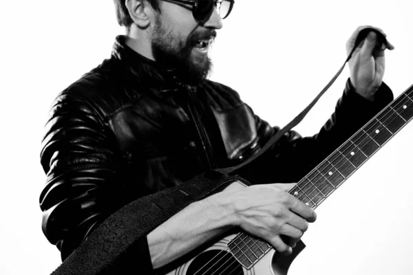 Mężczyzna gra na gitarze w czarnej skórzanej kurtce z okularami przeciwsłonecznymi na jasnym tle — Zdjęcie stockowe