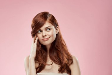 Uzun, güzel saçları olan, saç stili yapan, çekici, çıplak omuzları olan, pembe arka planı olan güzel bir kadın.