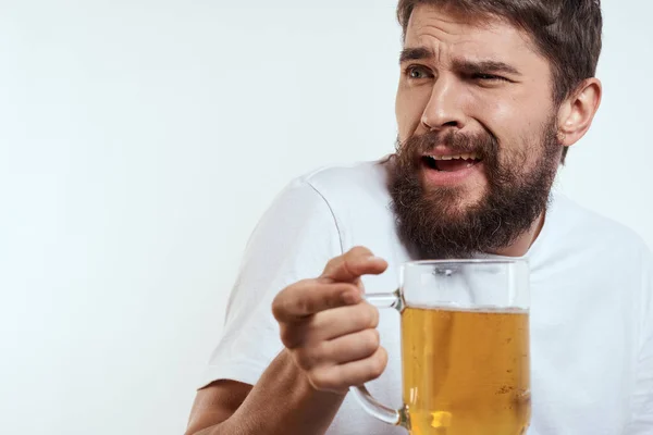 Homme avec une tasse de bière dans ses mains et un t-shirt blanc fond clair moustache barbe émotions modèle — Photo