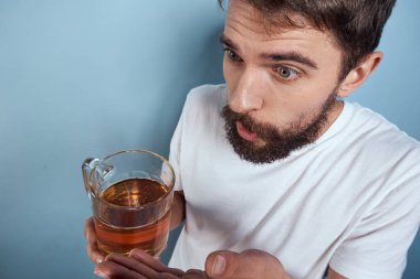 Beyaz tişörtlü, bira kupalı, sarhoş, mavi arka planlı neşeli bir adam.
