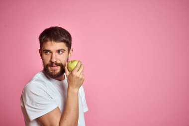 Pembe arka planda elmalı tatlı bir adam. Elleri kesilmiş beyaz tişörtlü, Uzay Kopyası.