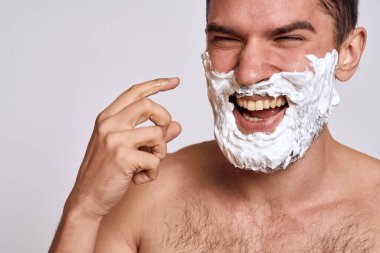 Yüzünde beyaz tıraş köpüğü olan yakışıklı bir adam ve jilet gibi omuzları olan temiz bir cilt.