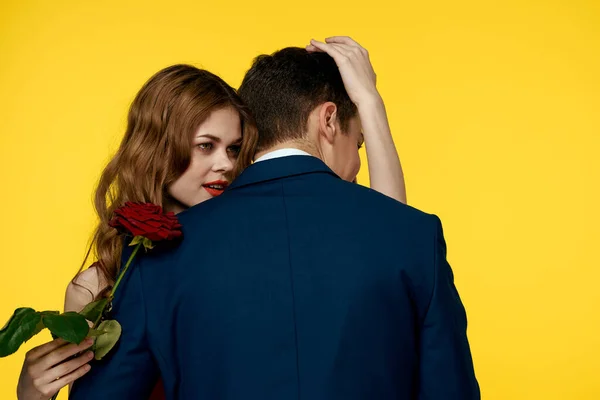 Amanti uomo e donna con una rosa rossa nelle loro mani abbracciando su uno sfondo giallo relazione sentimentale amore famiglia — Foto Stock