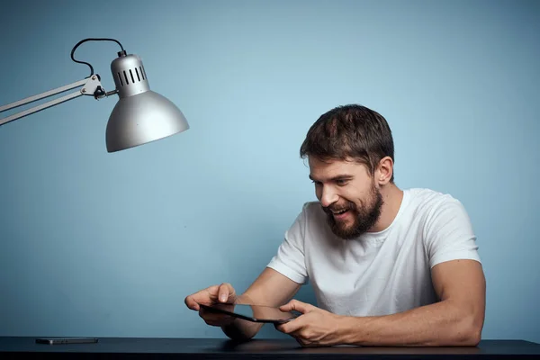 Homem com tablet à mesa dentro de casa e lâmpada escritório freelancer fundo azul — Fotografia de Stock