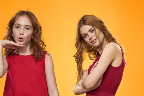 Mulher feliz e menina em vestido vermelho estão se divertindo em um fundo amarelo emoções da moda irmãs diversão espaço de cópia. — Fotografia de Stock