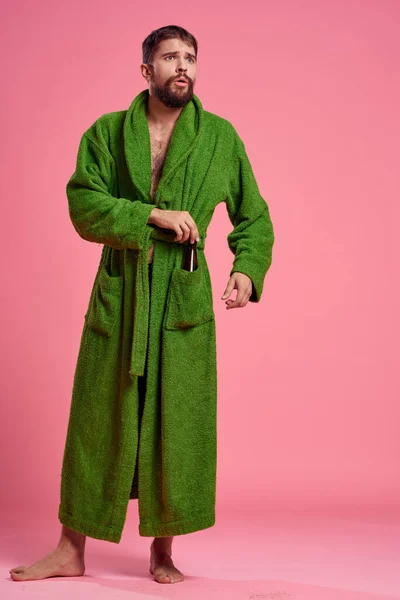 An emotional man in a green robe in full growth on a pink background gestures with his hands to the model — Stock Photo, Image