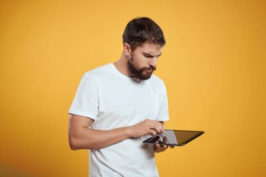 Beyaz tişörtlü, sarı arka planda tabletli bir adam. Yeni teknoloji işadamı ekranda dokunuyor.