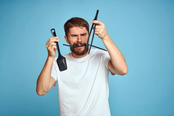 Bearded man with tools for cooking on a blue background and a white T-shirt shovel