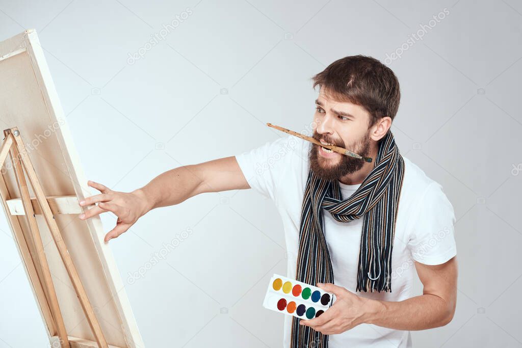 A man artist paints on an easel a brush and paint in the hands of a hobby creativity light background