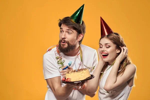 Glad man och kvinna med födelsedagstårta mössa fest gul bakgrund — Stockfoto