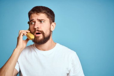 Muzlu bir adam, beyaz bir tişörtle mavi arka planda telefonla iletişim kurarken yakalanır.