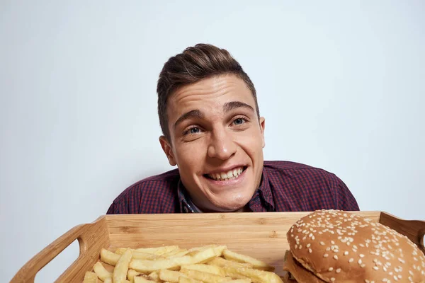 Ein Mann hält vor sich eine Palette Fast Food Pommes Hamburger in Großaufnahme — Stockfoto
