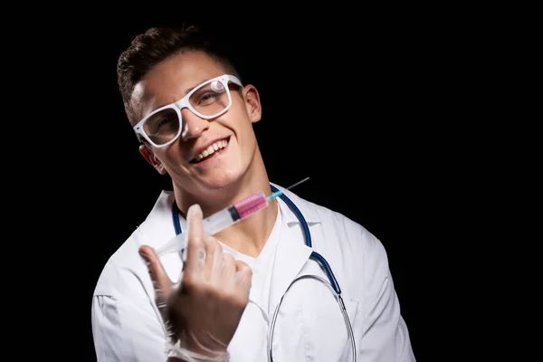 Medico con liquido in una siringa su uno sfondo nero e uno stetoscopio intorno al collo vista ritagliata — Foto Stock