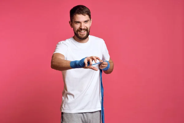 Uomo in t-shirt bianca si lega la mano con una benda arti marziali sfondo rosa — Foto Stock